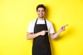 Friendly waiter pointing fingers right, showing your logo or promo offer, wearing black apron uniform, standing over