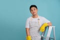 Friendly young Asian male repairman sitting on the stairs isolated on light blue background Royalty Free Stock Photo