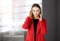 Friendly young business woman or female student dressed in red coat is standing straight and looking at camera in a Royalty Free Stock Photo