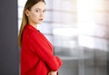 Friendly young business woman or female student dressed in red coat is standing straight and looking at camera in a Royalty Free Stock Photo