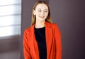 Friendly young business woman or female student dressed in red coat is standing straight and looking at camera. Urban Royalty Free Stock Photo