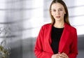 Friendly young business woman or female student dressed in red coat is standing straight and looking at camera. Urban Royalty Free Stock Photo