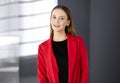 Friendly young business woman or female student dressed in red coat is standing straight and looking at camera. Urban Royalty Free Stock Photo