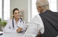 Friendly young female doctor consults senior male patient and makes entries in his medical card. Royalty Free Stock Photo