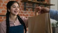 Friendly young indian woman waitress barista giving takeaway food bag to customer female seller cafe employee in apron Royalty Free Stock Photo