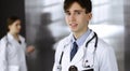 Friendly young male doctor standing with clipboard in modern clinic. Female colleague is busy with filling up of