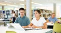 Friendly young woman offering assistance to male friend studying, finding information at library Royalty Free Stock Photo