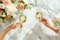 Friends clinking glasses, top view. White wine, flowers around on marble table in the restaurant. Wedding celebration, party,