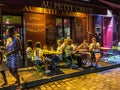 Friends eat at sidewalk cafe in yellow light of evening on Montmartre in Paris, France