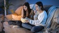 Friends eating popcorn from big bowl while watching TV show in living room at night Royalty Free Stock Photo