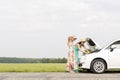 Friends examining broken down car on country road against clear sky Royalty Free Stock Photo