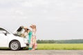 Friends examining broken down car on country road against clear sky Royalty Free Stock Photo