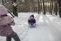 Friends have fun in wonderland, little girl pulls a sledge with brother across winter forest Royalty Free Stock Photo