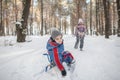 Friends have fun in wonderland, little girl pulls a sledge with brother across winter forest Royalty Free Stock Photo