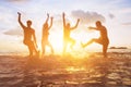 Friends having fun on the beach, silhouettes at sunset in water