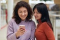 Friends having fun with smart phone, looking at mobile phones screen with happy expression and laughing, females wearing sweaters Royalty Free Stock Photo