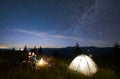 Friends travellers spending time in the mountains sitting around bonfire in camping under beautiful starry sky Royalty Free Stock Photo