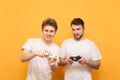 Friends with joysticks in their hands are on a yellow background, looking into the camera and playing video games. Two people play Royalty Free Stock Photo