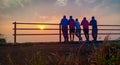 Friends looking at sunrise by residing on railing with neutral emotions. Royalty Free Stock Photo