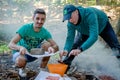 Friends making barbecue outdoors in woods.