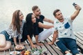 Friends making selfie sitting on pier with lake background while Royalty Free Stock Photo