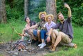 Friends near bonfire enjoy vacation and roasted food. Man taking photo near bonfire nature background. Tourists sit log