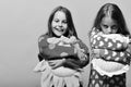 Friends in pink pajamas isolated on pink background. Girls with loose hair hug their pillows. Childhood and friendship