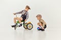 Friends playing. Boys, childred in retro clothes riding vintage bicycle over grey studio background. Concept of game Royalty Free Stock Photo