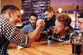 Friends plays arm wrestling. Group of people together indoors in the pub have fun at weekend time Royalty Free Stock Photo