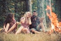 Friends relax at bonfire flame with sparks in vintage style. People camping at fire in forest. Women and bearded man at Royalty Free Stock Photo