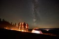 Friends resting beside camp, campfire under night starry sky Royalty Free Stock Photo