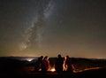 Friends resting beside camp, campfire under night starry sky Royalty Free Stock Photo