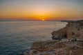 Friends seated on cliff and watching Sunset at Atlantic ocean coast, in Carvoeiro beach clifs, Algarve, Portugal