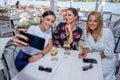 Friends sit at a table with a glass of wine drinking, talking, and taking selfies. Royalty Free Stock Photo