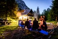 Friends sitting around bonfire in the woods and vacation house. Royalty Free Stock Photo