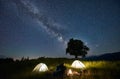 Friends travellers spending time in the mountains sitting around bonfire in camping under beautiful starry sky Royalty Free Stock Photo