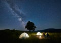 Friends travellers spending time in the mountains sitting around bonfire in camping under beautiful starry sky Royalty Free Stock Photo