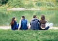 Friends sitting on grass by lake in park back view Royalty Free Stock Photo