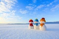 Friends snowman in red, blue, yellow hats and scarfs. Nice winter scenery with mountains, field in snow. Orange sunset background. Royalty Free Stock Photo