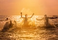 Friends splashing water in the sea at sunset.