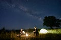 Friends travellers spending time in the mountains sitting around bonfire in camping under beautiful starry sky Royalty Free Stock Photo