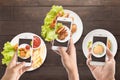 Friends using smartphones to take photos of sausage, pork chop,