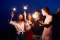 Friends walking, dancing and having fun during night party at the seaside with bengal sparkler lights in their hands