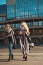 Friends walking together. Two beautiful women spend time on the street holding coffee and smiling.