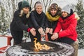 friends in winter coats sitting fire in forest