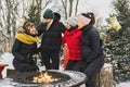 friends in winter coats sitting fire in forest