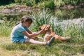 Friendship of animals and children, people. Caucasian girl sits on the bank of a pond, river and plays with a dog puppy, labrador Royalty Free Stock Photo
