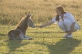 Friendship between girl and grey baby donkey on the sunset pasture