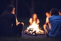 Friendship group sit round a bright campfire at night