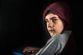 Frightened and angry boy in the hood, a young hacker, looks around, holding the keyboard in his hand